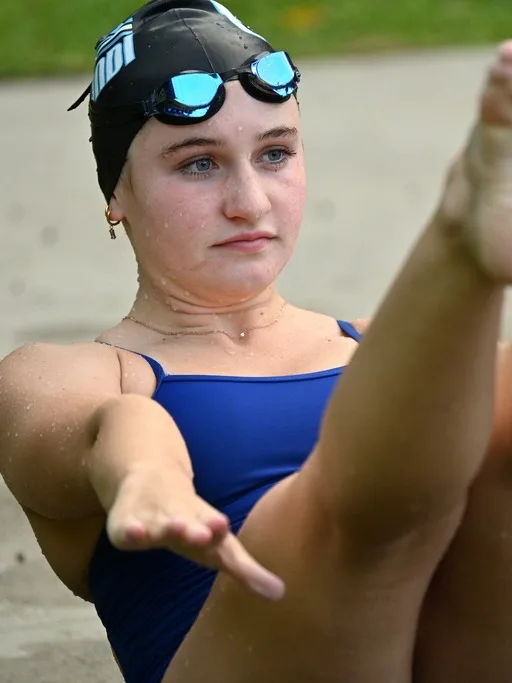 A swimmer in cap and goggles holding a seated pike position during a dryland session
